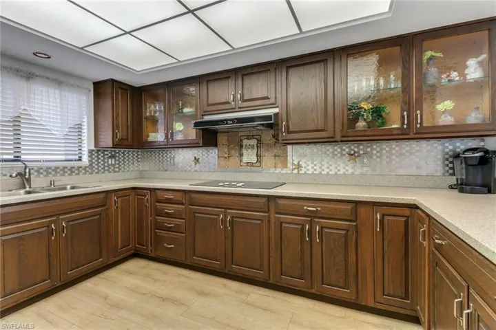 Kitchen featuring light hardwood / wood-style floors, tasteful backsplash, dark brown cabinets, black electric stovetop, and sink