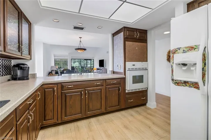 Kitchen with hanging light fixtures, white appliances, dark brown cabinets, light hardwood / wood-style flooring, and decorative backsplash
