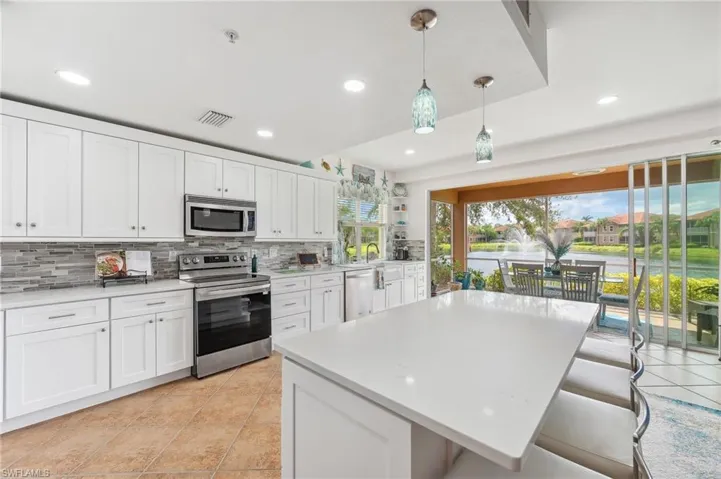 Kitchen featuring white cabinets, decorative backsplash, appliances with stainless steel finishes, and decorative light fixtures