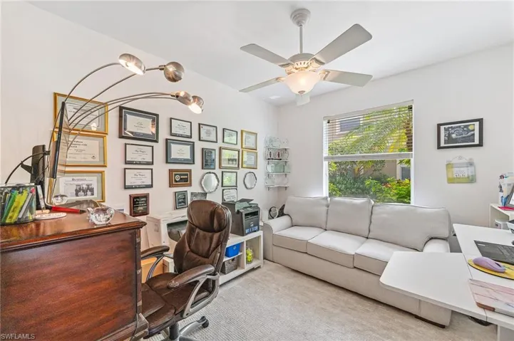 Carpeted office space with ceiling fan with notable chandelier