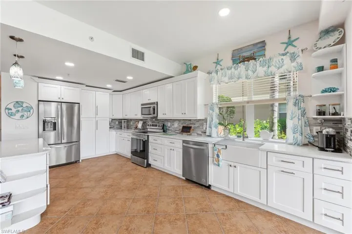 Kitchen featuring appliances with stainless steel finishes, light tile patterned floors, decorative light fixtures, backsplash, and white cabinets