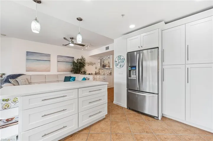 Kitchen with pendant lighting, vaulted ceiling, light tile patterned floors, stainless steel fridge with ice dispenser, and white cabinetry