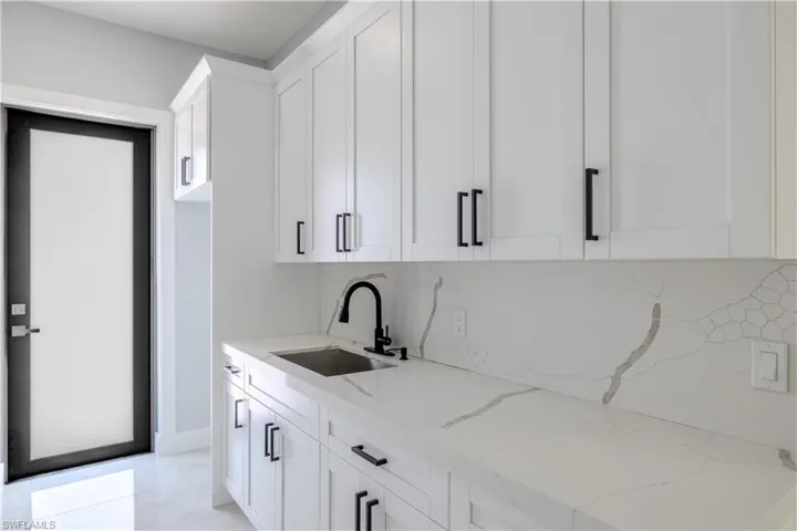 Bar area with light stone countertops, white cabinets, and backsplash