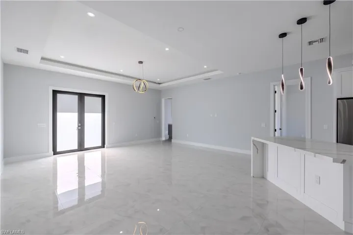 Unfurnished living room with light marble finish floors, french doors, recessed lighting, and a tray ceiling