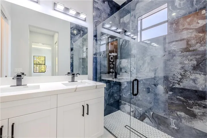Full bath featuring a marble finish shower and double vanity