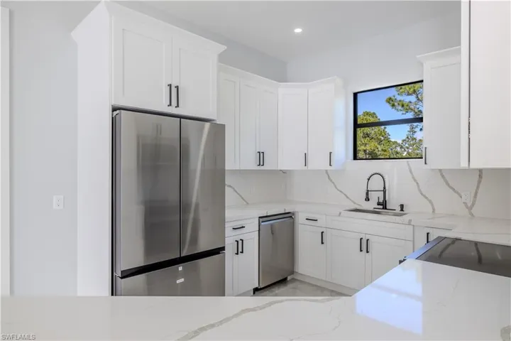 Kitchen featuring light stone countertops, appliances with stainless steel finishes, white cabinetry, backsplash, and recessed lighting