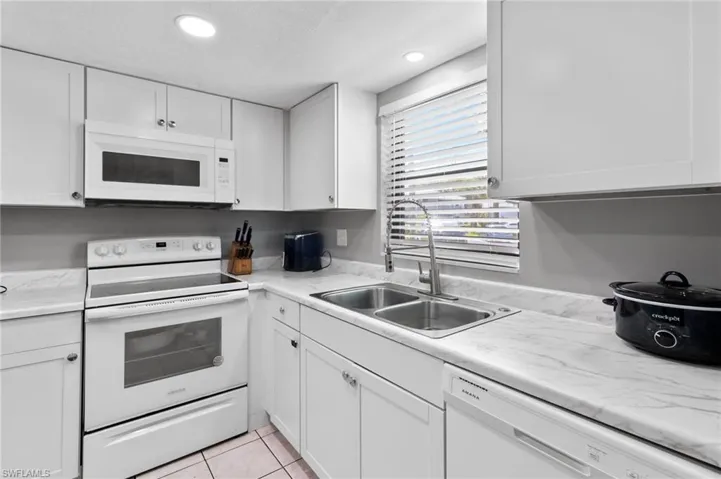 Kitchen featuring sink, white appliances, white cabinetry, and light tile floors