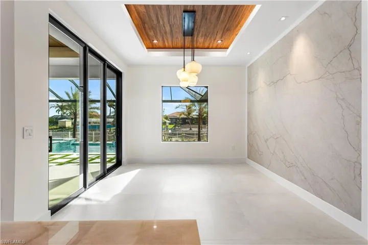 SOPHISTICATED FORMAL DINING ROOM w/ NATURAL STONE FEATURE WALL, FLAT WOODEN CEILING, designer lighting & 9-ft-tall, TINTED SLIDING DOORS leading to SCREENED LANAI & large PICTURE WINDOW offer views of POOL/SPA/WATERFRONT CANAL