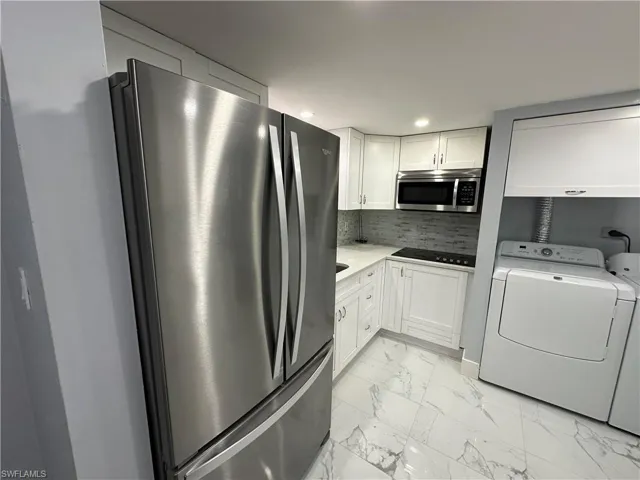 Kitchen with tasteful backsplash, marble finish floor, washing machine and dryer, white cabinets, and appliances with stainless steel finishes