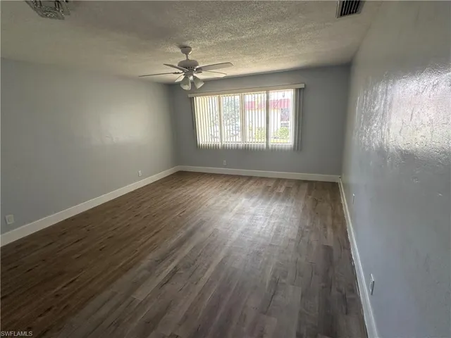 Empty room with baseboards, ceiling fan, visible vents, and dark wood finished floors