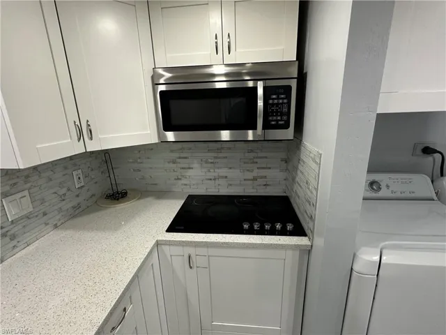 Kitchen featuring black electric stovetop, white cabinets, washer / dryer, and stainless steel microwave