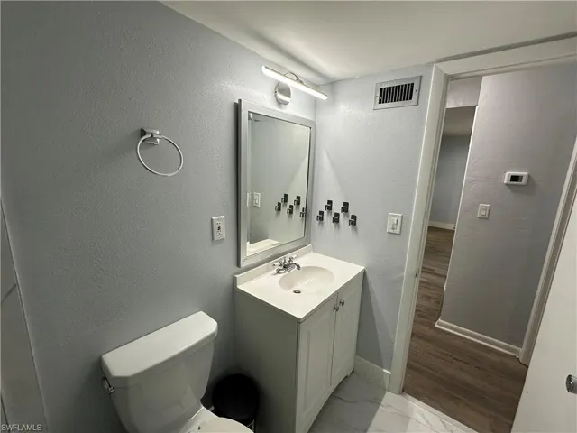 Half bathroom featuring toilet, vanity, marble finish floor, baseboards, and visible vents