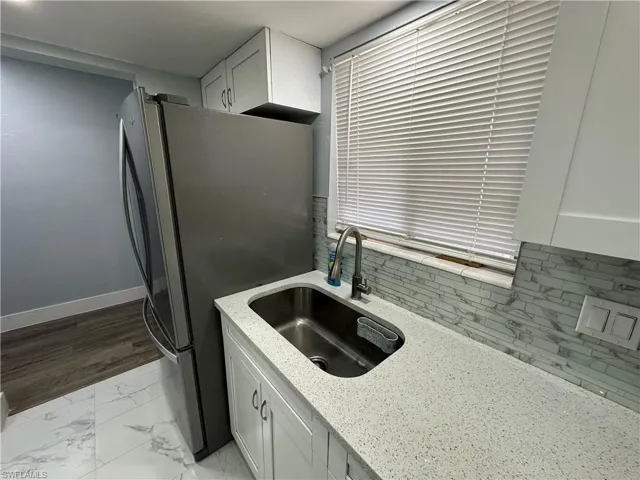 Kitchen featuring a sink, freestanding refrigerator, light stone countertops, marble finish floor, and baseboards