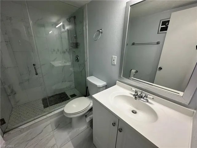 Full bath featuring a marble finish shower, marble finish floor, toilet, and vanity