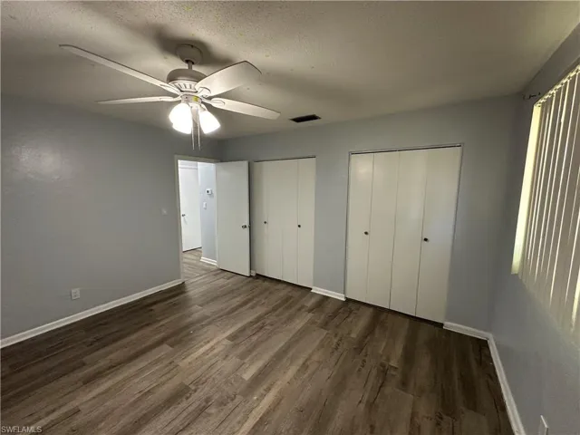 Unfurnished bedroom with a ceiling fan, wood finished floors, a textured ceiling, multiple closets, and baseboards