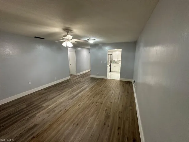 Unfurnished room with a textured ceiling, visible vents, baseboards, a ceiling fan, and dark wood-type flooring