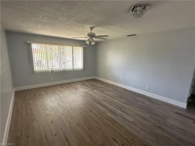 Empty room with baseboards, a textured ceiling, dark wood finished floors, visible vents, and ceiling fan