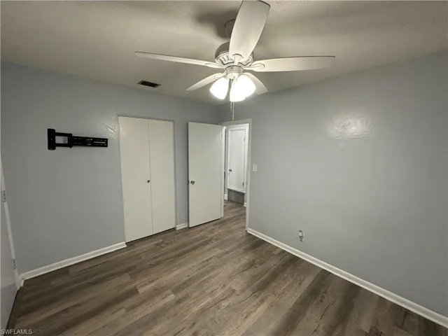 Unfurnished bedroom with baseboards, visible vents, dark wood-type flooring, and a ceiling fan