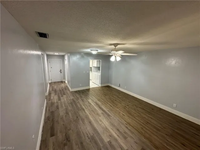Empty room with a ceiling fan, a textured ceiling, dark wood-style floors, baseboards, and visible vents