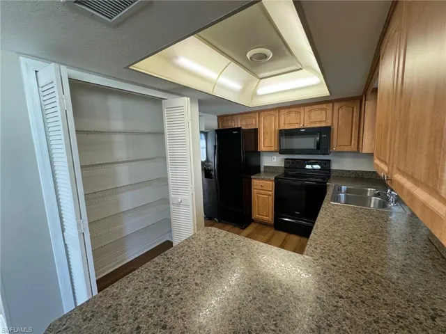 Kitchen featuring a textured ceiling, black appliances, sink, and wood-type flooring
