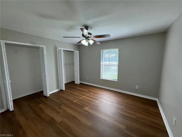 Guest bedroom 1 with a textured ceiling, ceiling fan, dark hardwood / wood-style floors, and multiple closets