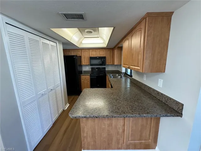Kitchen featuring black appliances, dark hardwood / wood-style flooring, kitchen peninsula, sink, and a tray ceiling