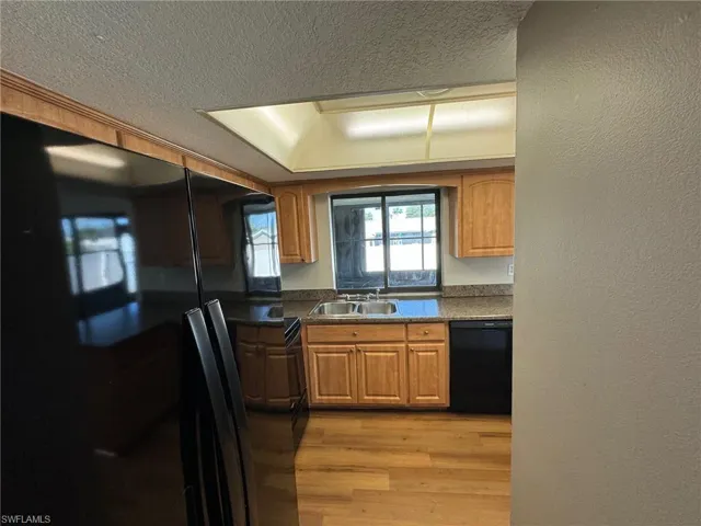 Kitchen with light wood-type flooring, black appliances, sink, and a textured ceiling