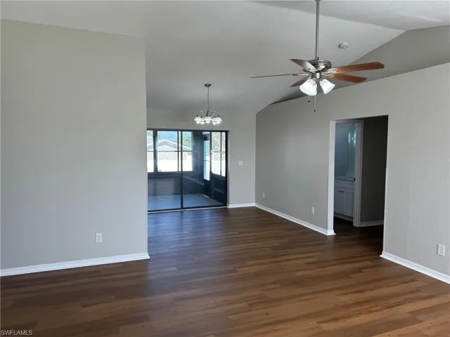 dining/living room featuring ceiling fan with notable chandelier, lofted ceiling, and dark hardwood / wood-style floors