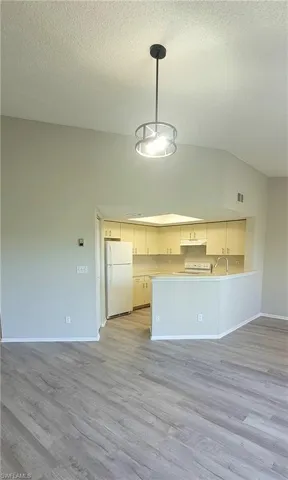 Kitchen with pendant lighting, white appliances, lofted ceiling, and light hardwood / wood-style floors