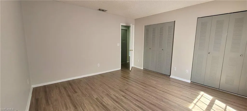 Unfurnished bedroom featuring two closets, a textured ceiling, and hardwood / wood-style flooring
