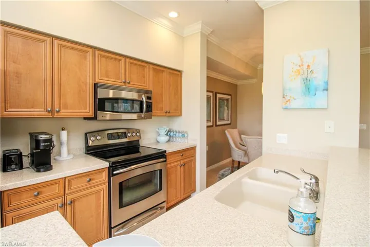 Kitchen with light countertops, ornamental molding, appliances with stainless steel finishes, a sink, and brown cabinetry