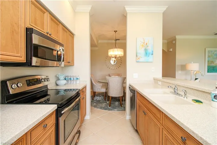Kitchen with ornamental molding, a sink, a notable chandelier, and appliances with stainless steel finishes