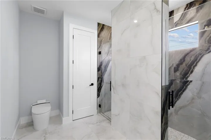 Bathroom with a shower with door, tile patterned flooring, and toilet