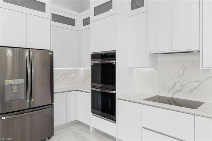 Kitchen with light stone counters, tasteful backsplash, stainless steel appliances, and white cabinets