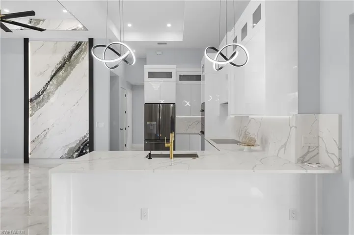 Kitchen featuring stainless steel appliances, sink, hanging light fixtures, light stone countertops, and white cabinetry