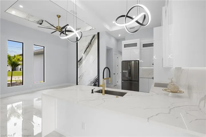 Kitchen with sink, light stone counters, hanging light fixtures, stainless steel refrigerator with ice dispenser, and white cabinetry
