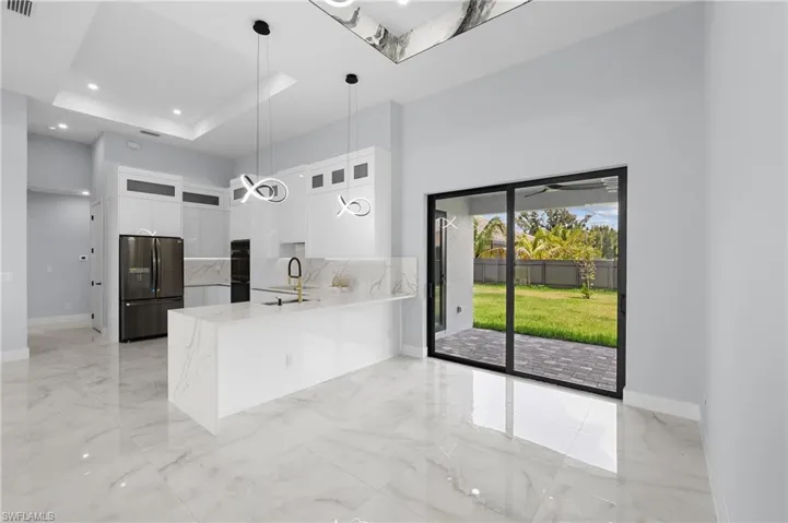 Kitchen featuring white cabinetry, backsplash, a tray ceiling, pendant lighting, and stainless steel fridge