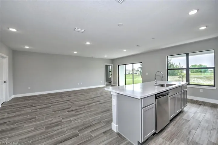Kitchen with dishwasher, an island with sink, sink, gray cabinets, and light wood-type flooring