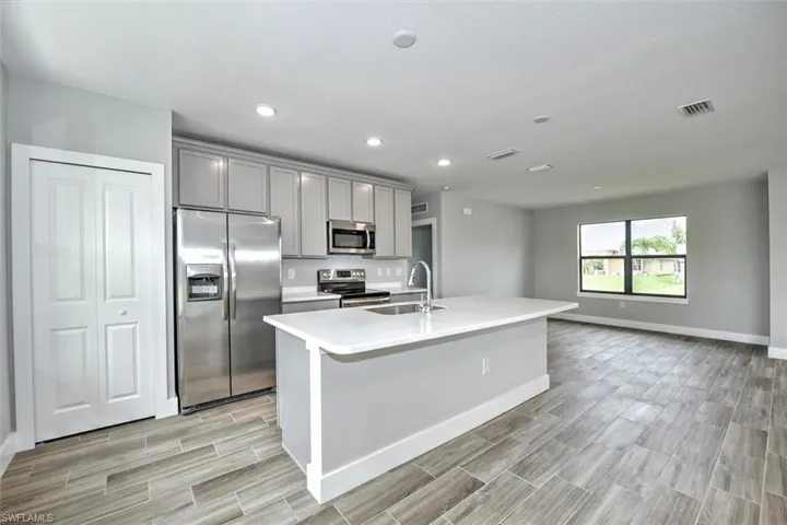 Kitchen with stainless steel appliances, light hardwood / wood-style floors, sink, gray cabinets, and an island with sink