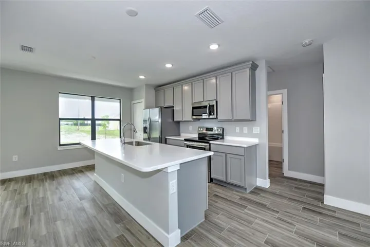Kitchen with a kitchen island with sink, light hardwood / wood-style flooring, sink, appliances with stainless steel finishes, and gray cabinetry
