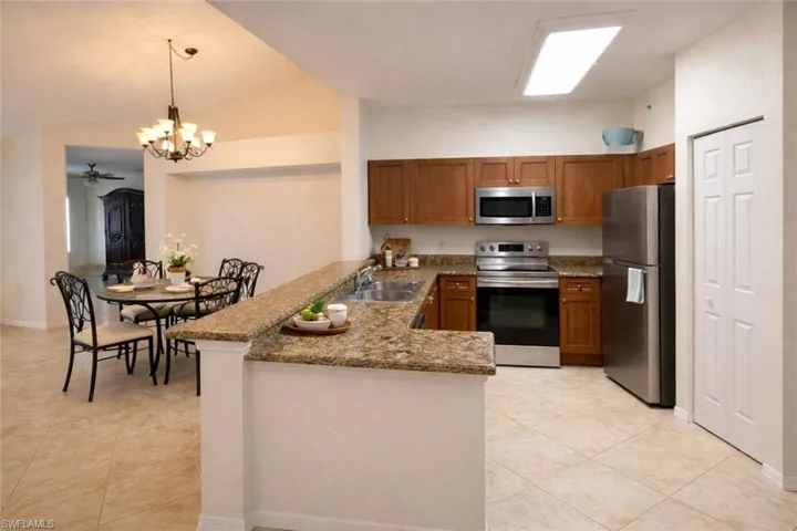 Kitchen with stainless steel appliances, a peninsula, wood finish cabinetry, dark stone countertops, and a chandelier