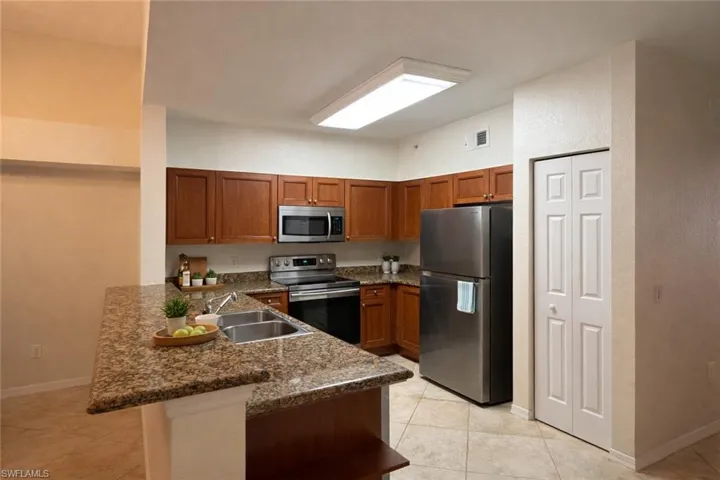 Kitchen featuring a peninsula, stainless steel appliances, wood finish cabinetry, dark stone countertops, and light tile patterned flooring