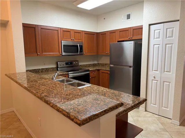 Kitchen with a textured wall, stainless steel appliances, dark stone countertops, wood finish cabinetry, and a peninsula