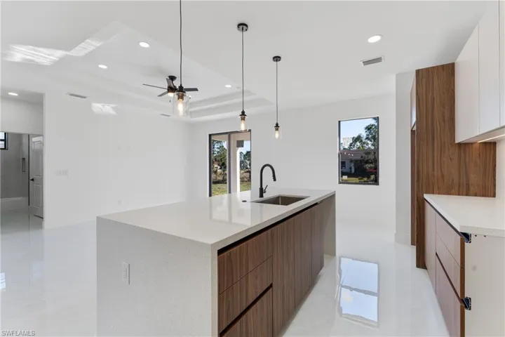 Kitchen with decorative light fixtures, white cabinetry, sink, a large island, and a raised ceiling