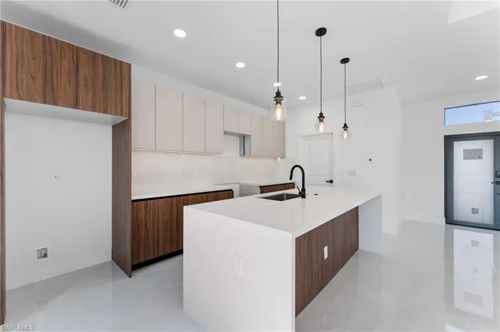 Kitchen featuring sink, hanging light fixtures, an island with sink, decorative backsplash, and white cabinets