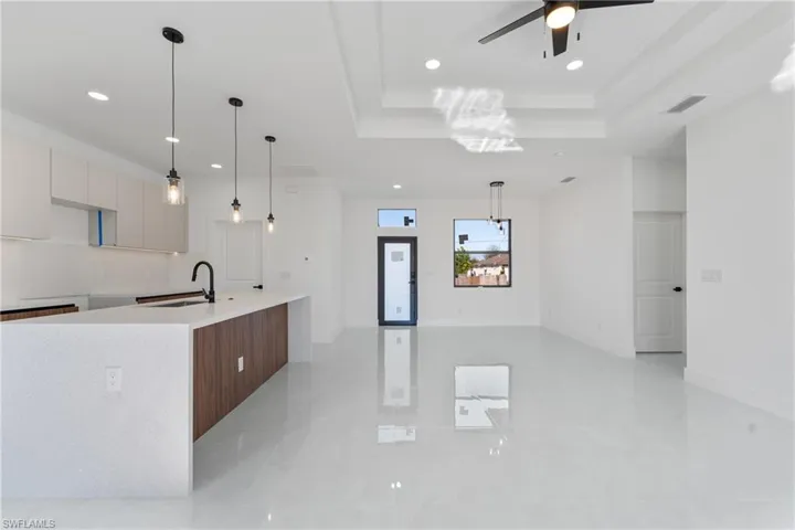 Kitchen with sink, ceiling fan, hanging light fixtures, a center island with sink, and a raised ceiling