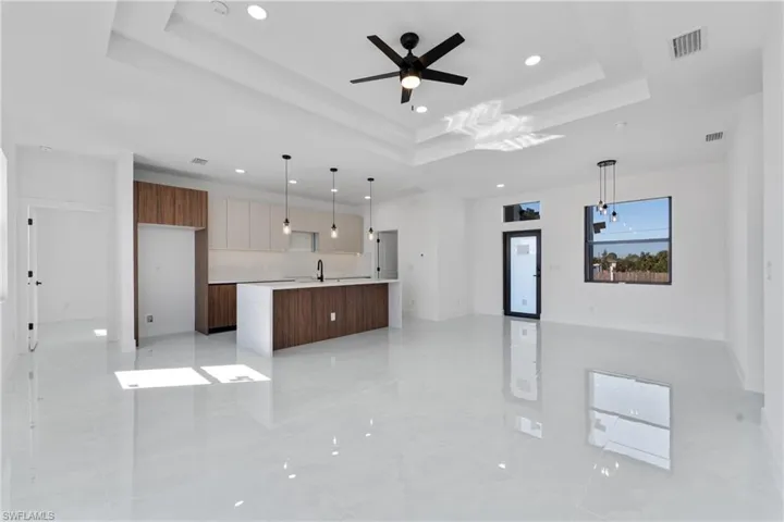 Kitchen with sink, a tray ceiling, pendant lighting, ceiling fan, and a kitchen island with sink