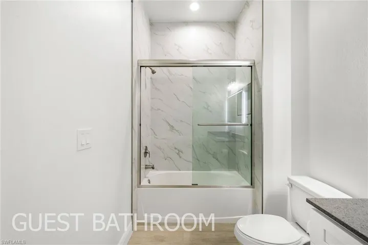 Full bathroom featuring vanity, toilet, hardwood / wood-style flooring, and bath / shower combo with glass door