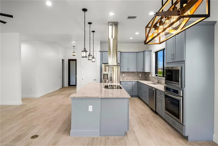 Kitchen featuring gray cabinets, light wood-type flooring, stainless steel appliances, a center island, and sink