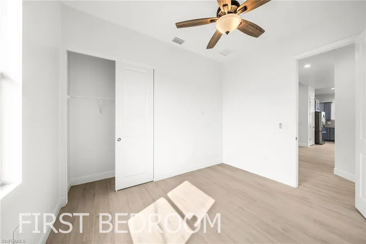 Unfurnished bedroom with stainless steel fridge, light hardwood / wood-style flooring, ceiling fan, and a closet